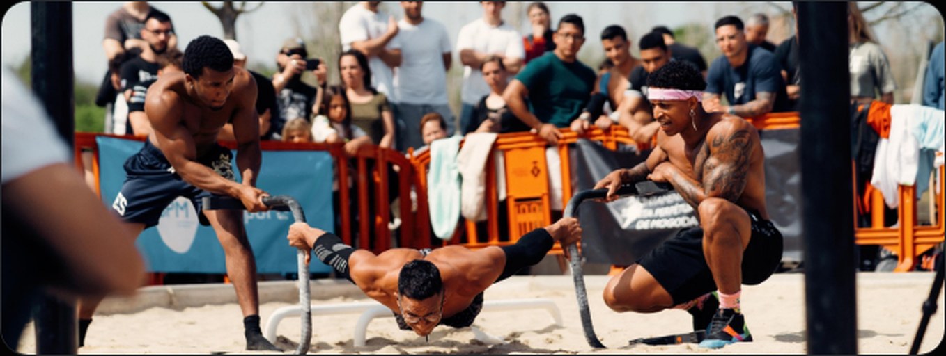 Dos atletas de calistenia compitiendo sobre anillas en la playa ante el público